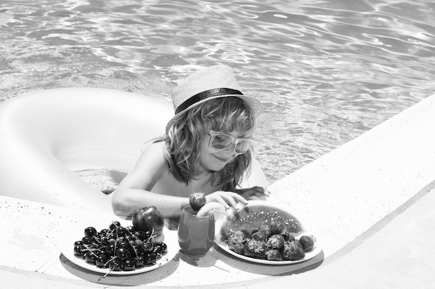 Bambino che mangia frutta vicino alla piscina durante le vacanze estive I bambini mangiano frutta all'aperto Frutti sani per i bambini