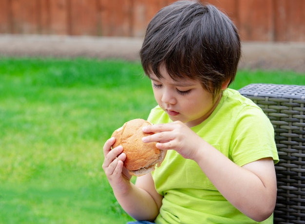 Bambino che mangia hamburger seduto in giardino