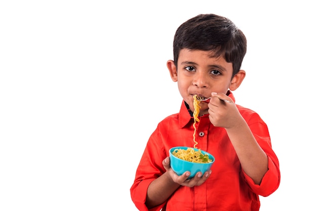 Bambino che mangia pasta deliziosa, bambino indiano che mangia tagliatelle con la forcella su cenni storici bianchi