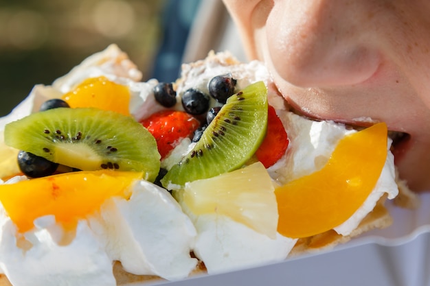 Bambino che mangia torta di waffle fresca con frutta e panna montata in vacanza.