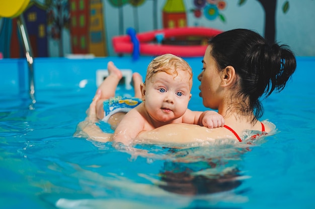 Bambino che nuota in piscina Insegnare a un neonato a nuotare in piscina con un allenatore