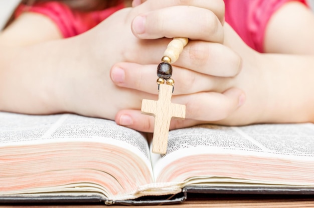 Bambino che prega sopra la Bibbia aperta con il rosario in mano