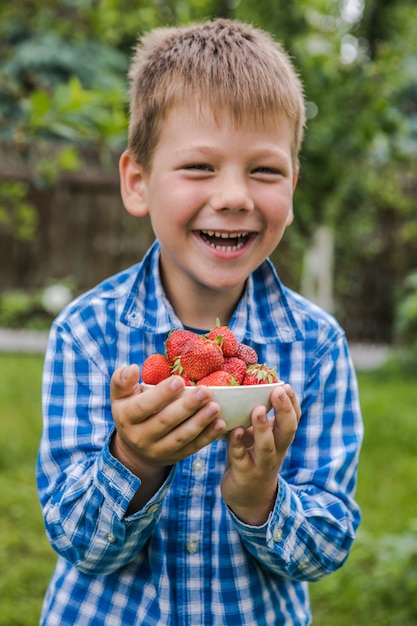 Bambino che raccoglie fragola sul campo dell'azienda agricola di frutta il giorno di estate soleggiato. I bambini tengono in mano una fragola biologica matura fresca fresh