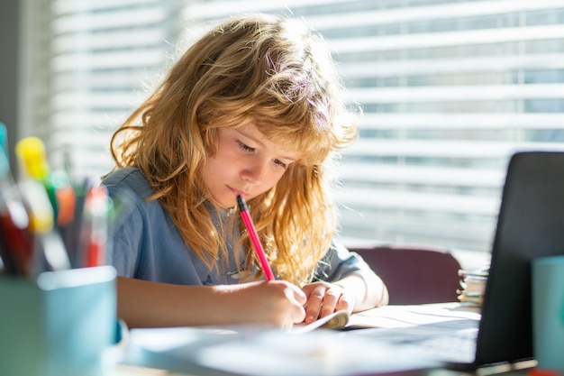 Bambino che scrive a scuola Ragazzo di scuola che prende appunti sul quaderno durante la lezione online sul laptop a casa c