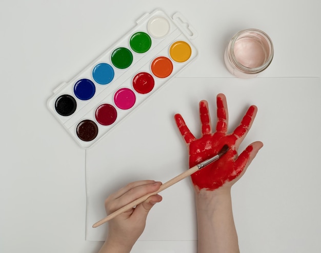 Bambino che si dipinge la mano con vernice rossa e pennello Pittura con le dita o arte terapia per bambini Attività divertenti per i più piccoli