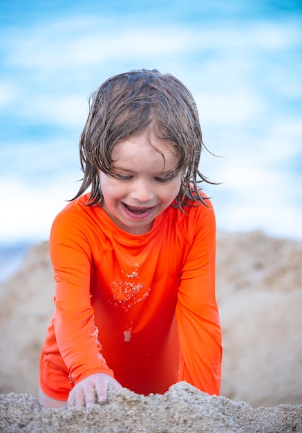 Bambino che si diverte al bambino della spiaggia di sabbia che fa un castello di sabbia sul mare