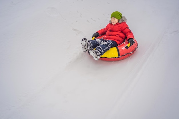 Bambino che si diverte sul tubo di neve Il ragazzo sta cavalcando un tubo Divertimento invernale per i bambini