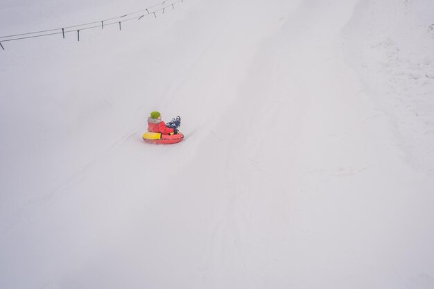 Bambino che si diverte sul tubo di neve Il ragazzo sta cavalcando un tubo Divertimento invernale per i bambini