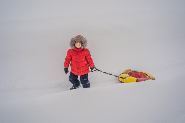 Bambino che si diverte sul tubo di neve Il ragazzo sta cavalcando un tubo Divertimento invernale per i bambini