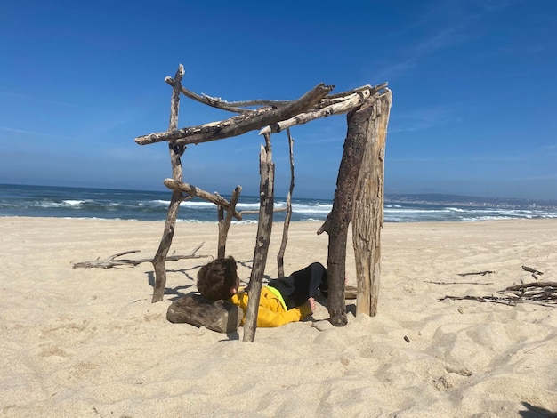Bambino che si rilassa su una casa sulla spiaggia in legno fatta da sé sulla sabbia. Giorno soleggiato