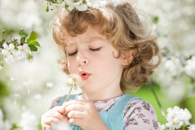 Bambino che soffia sul dente di leone su sfondo verde primavera