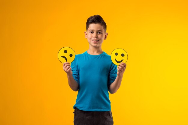 Bambino che tiene emoticon con emozioni felici e tristi