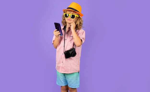 Bambino che tiene il telefono cellulare e la macchina fotografica viaggio fotografo moda ragazzo con cappello estivo camicia e s