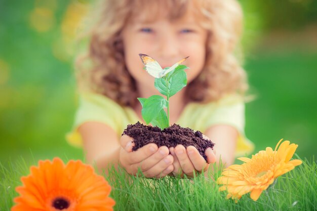 Bambino che tiene in mano una pianta giovane su sfondo verde primaverile Concetto di ecologia e giornata della Terra