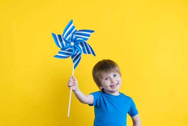 Bambino che tiene turbina eolica giocattolo contro la superficie gialla