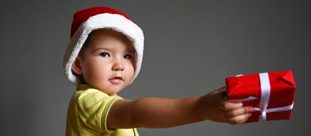 Bambino che tiene un regalo in un cappello di Natale. Foto di alta qualità