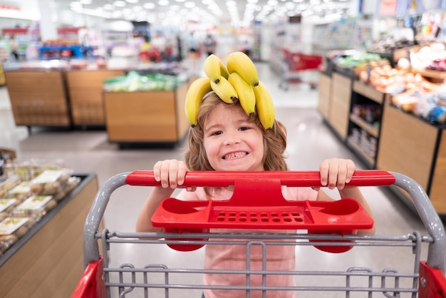 Bambino con carrello della spesa al supermercato o bambino del supermercato che acquista frutta di banana nel mercato alimentare