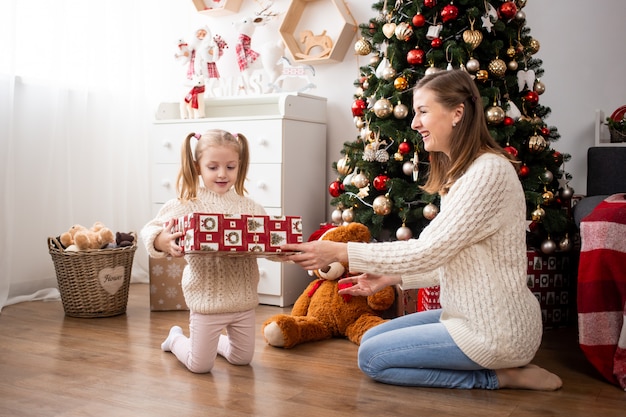 Bambino con confezione regalo e sua madre a casa vicino all'albero di Natale