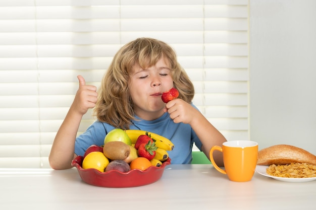 Bambino con frutta estiva alla fragola ragazzo divertente che fa colazione latte verdure e frutta salute