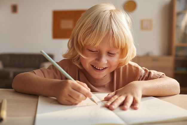 Bambino con i capelli biondi che scrive il rapporto nel taccuino che fa i compiti dopo la scuola