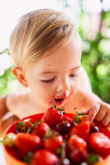 Bambino con la bocca aperta raggiunge un vaso di fragole