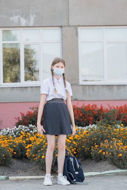 Bambino con maschera facciale che torna a scuola dopo la quarantena e il blocco del covid-19. Torna a scuola studentessa universitaria che indossa una maschera covid che cammina nel campus con zaino, libri e laptop