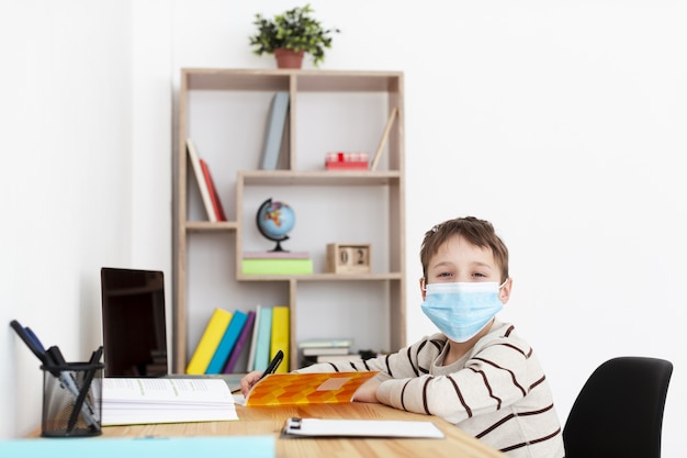 Bambino con maschera medica in posa mentre si fa i compiti
