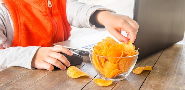 Bambino con patatine fritte dietro un computer. messa a fuoco selettiva.