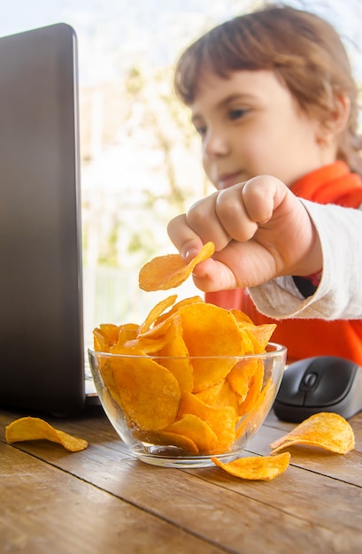 Bambino con patatine fritte dietro un computer