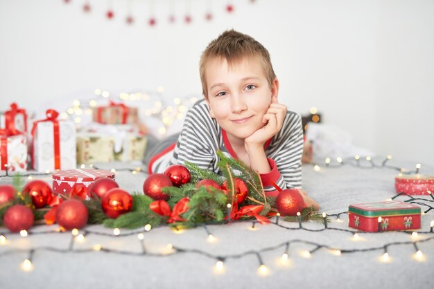 bambino con regali di Natale a casa sul letto con decorazioni natalizie