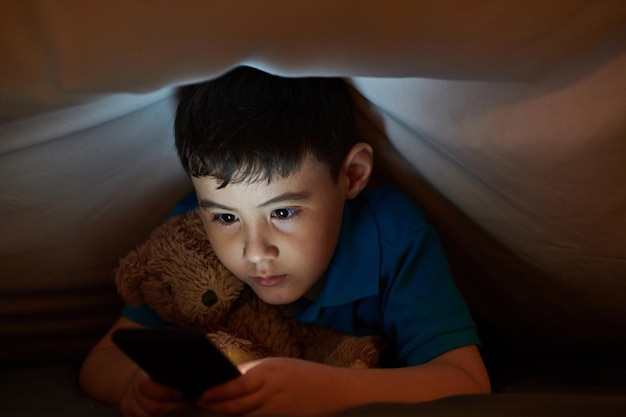 Bambino con smartphone sotto la coperta