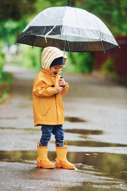 Bambino con stivali impermeabili gialli e con ombrello che gioca all'aperto dopo la pioggia