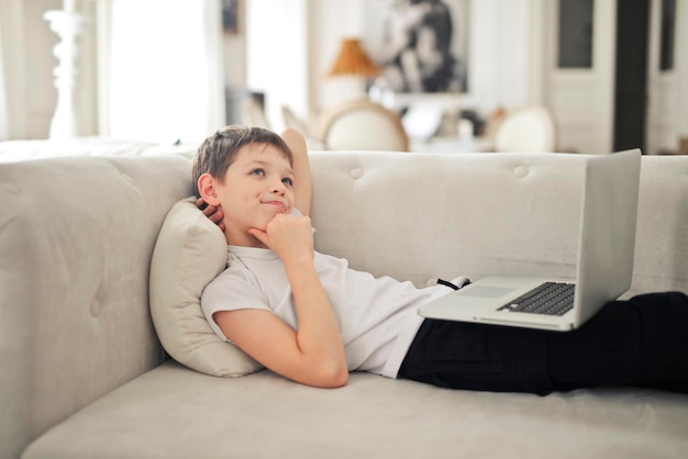 bambino con un computer in mano sdraiato su un divano