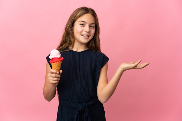 Bambino con un gelato alla cornetta sopra la parete rosa isolata che estende le mani a lato per invitare a venire