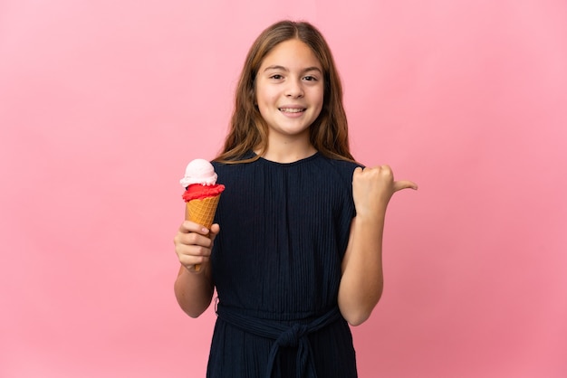 Bambino con un gelato alla cornetta su sfondo rosa isolato che punta al lato per presentare un prodotto