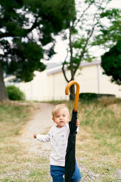 Bambino con un portaombrelli piegato sul sentiero in un parco verde