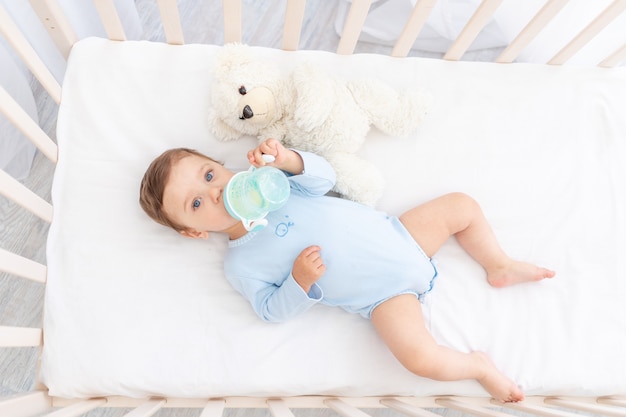 Bambino con una bottiglia di latte in mano nella culla che mangia, concetto di pappe