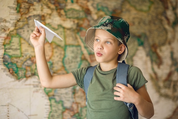 Bambino con uno zaino sulla schiena, sogna di viaggiare, lancia in aria un aeroplano di carta