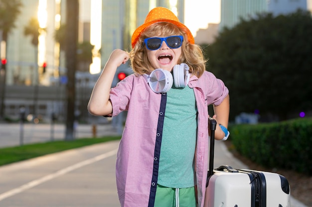 Bambino con valigia che va in vacanza Ragazzo turistico in viaggio per le vacanze concetto di bambini Ragazzo carino con valigia sullo sfondo della strada cittadina