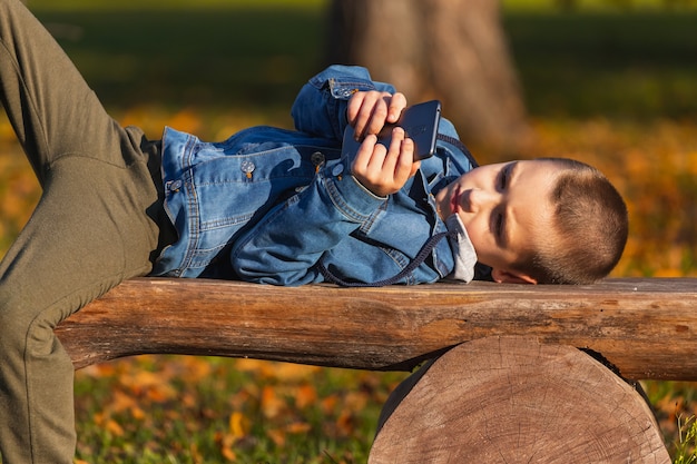 Bambino del ragazzino che gioca i giochi mobili sullo smartphone nel parco.