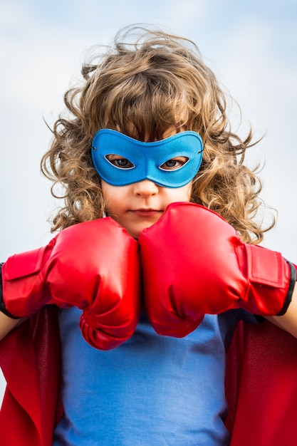 Bambino del supereroe che indossa i guantoni da pugile contro il fondo del cielo blu. Girl power e concetto di femminismo