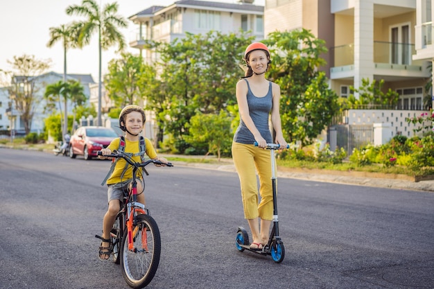 Bambino della scuola attivo e sua madre nel casco di sicurezza in sella a una bicicletta con zaino nella giornata di sole Bambino felice in bicicletta sulla strada per la scuola Modo sicuro per i bambini all'aperto a scuola