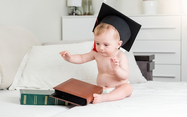 Bambino di 10 mesi con cappello da sparviere seduto con grandi libri