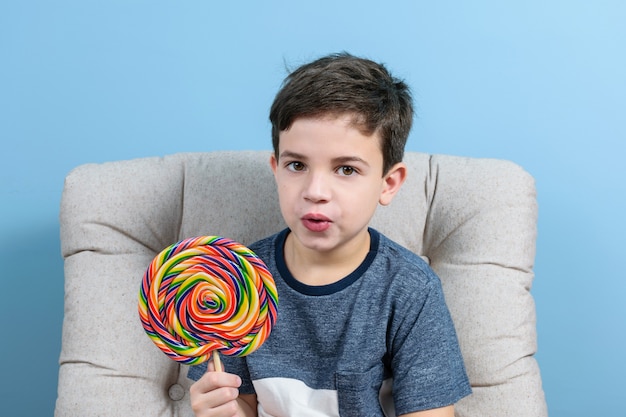 Bambino di 8 anni che guarda la telecamera con la bocca aperta e tiene in mano un grande lecca-lecca colorato.