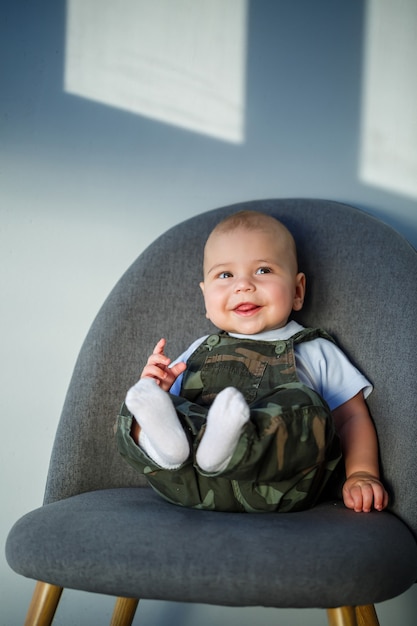 Bambino di 8 mesi in tuta, camicia bianca e calzini bianchi seduto su una sedia grigia