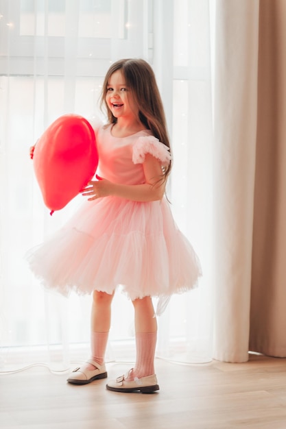 Bambino di San Valentino Una bambina con un vestito rosso tiene in mano una grande palla a forma di cuore