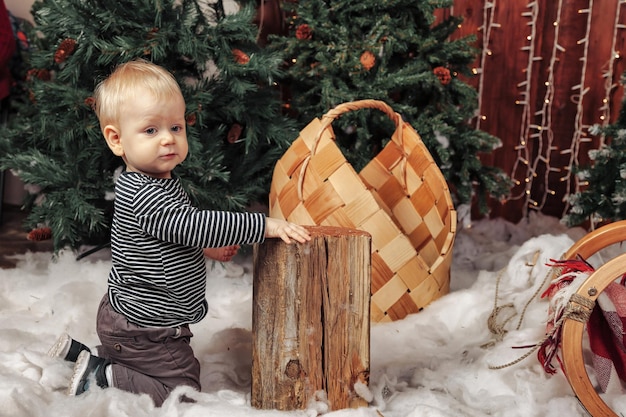 Bambino di un anno su soffice coperta bianca che gioca vicino all'albero di Natale. Ragazzo carino nel soggiorno decorato di Natale. Piccolo bambino che guarda lontano. Concetto di bambini felice anno nuovo. Copia spazio per il sito