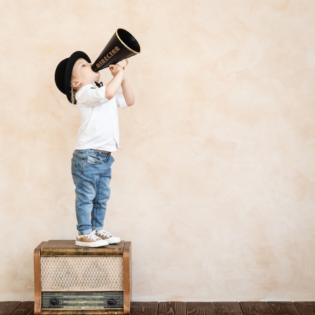 Bambino divertente che gioca in casa. Bambino che grida tramite il megafono vintage. Comunicazione e concetto di cinema retrò