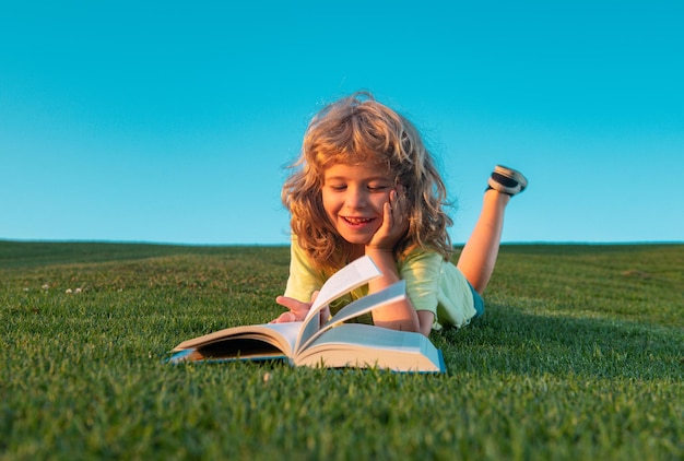 Bambino divertente che legge il libro nel parco di primavera libro di lettura del ragazzo del bambino che posa sull'erba nel campo sul bac del cielo