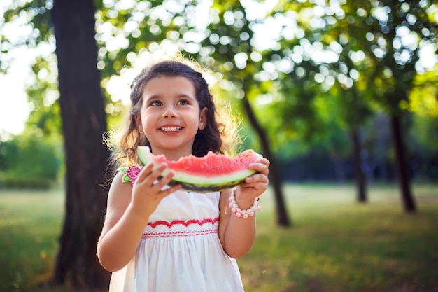 Bambino divertente che mangia anguria all'aperto nel parco estivo concentrarsi sugli occhi Cibo sano per bambini Stile di vita giovanile